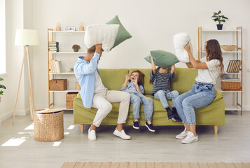 Happy family of four having fun on sofa at home. Excited cheerful mommy, daddy and two children having a pillow fight and laughing sitting on couch in modern cozy Scandinavian living room interior