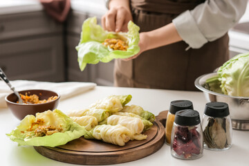 Woman preparing stuffed cabbage rolls on table in kitchen, closeup