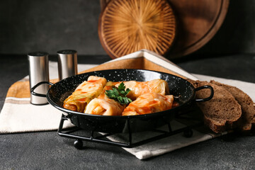 Frying pan with tasty stuffed cabbage rolls on dark background