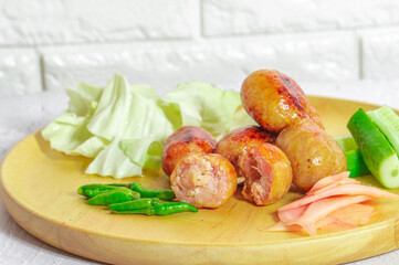 Isaan sausage is one of the famous dishes of Thailand, Isaan sausage is served in a wooden plate on a white table with chili and vegetables to eat together.