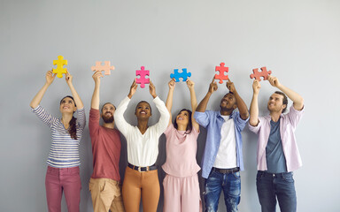 Group of happy smiling multiracial young people holding colorful puzzle pieces over their heads....