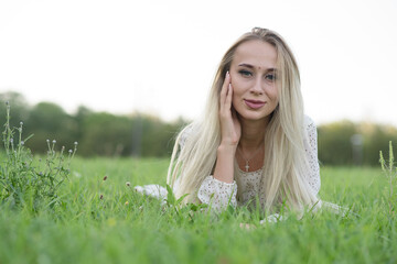 Happy and attractive blonde girl lying on the green grass on the lawn.