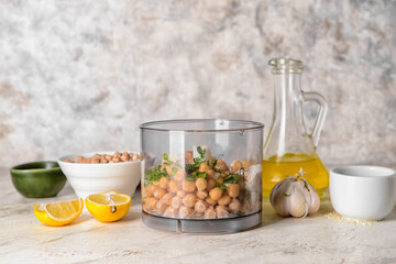 Blender with chickpea and ingredients for hummus on light background