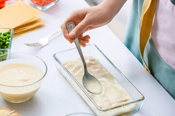 Woman preparing tasty vegetable lasagna at table in kitchen, closeup