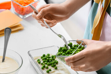 Woman preparing tasty vegetable lasagna at table in kitchen, closeup