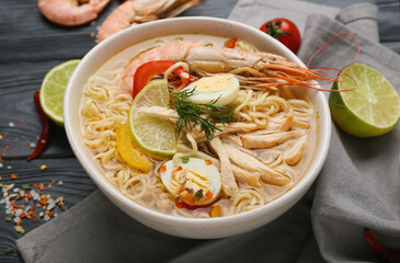 Bowl of tasty Thai soup with shrimps and chicken on dark wooden background