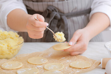 Woman preparing tasty dumplings on kitchen table, closeup