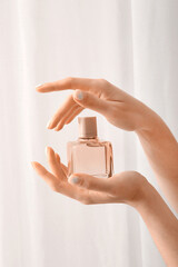 Woman with beautiful manicure holding bottle of perfume on light background