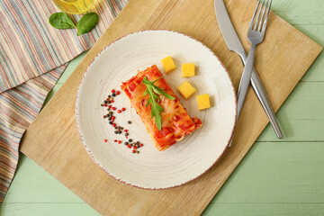 Plate with piece of tasty tomato lasagna on color wooden background