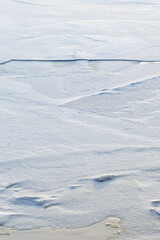 Snow on cracked ice on a frozen lake in the winter. Abstract full frame textured background. Copy space.