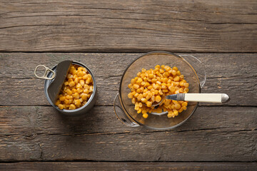 Tin can and bowl with corn kernels on wooden background