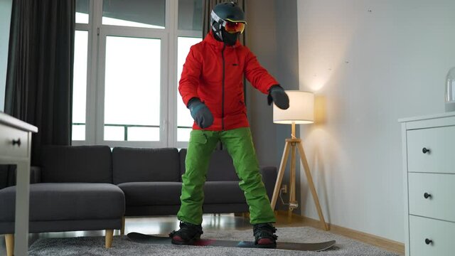 Funny video. Man dressed as a snowboarder depicts snowboarding on a carpet in a cozy room. Waiting for a snowy winter.