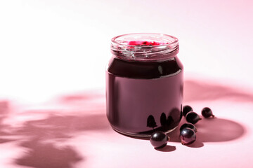 Jar with black currant jam on color background