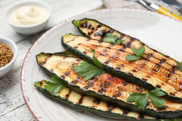 Plate with tasty grilled zucchini on light wooden background, closeup
