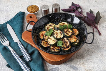 Frying pan with tasty grilled zucchini on light background
