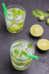 Cooling lemon drink with ice. Straw in glass. Two halves of lime on table.
