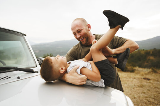 Dad and son playing on the hood of a car on road trip