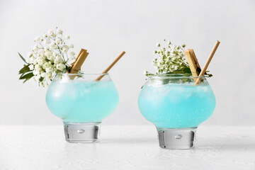 Glasses with tasty cocktail and beautiful gypsophila flowers on light background