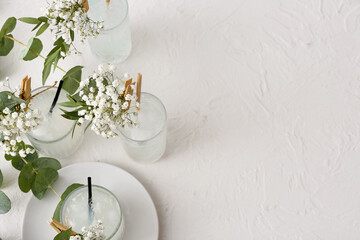 Glasses with tasty cocktail and beautiful gypsophila flowers on light background
