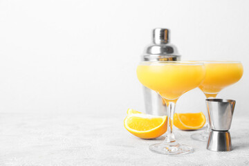 Glasses of orange margarita cocktail and shaker on light background