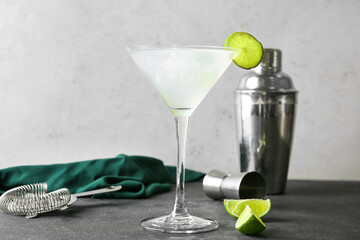 Glass of tasty margarita cocktail, shaker and strainer on table