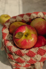 Red apple with a leaf in a knitted light bag on a light background in hard midday sunlight.