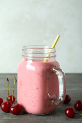 Glass jar of cherry smoothie and ingredients on gray textured table