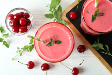 Glasses of cherry smoothie and ingredients on white wooden table
