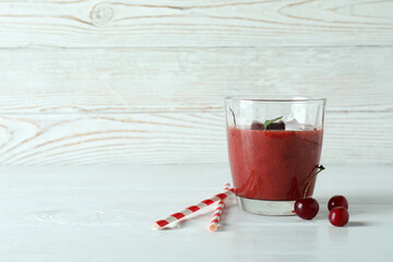Glass of cherry smoothie, straws and ingredients on white wooden table