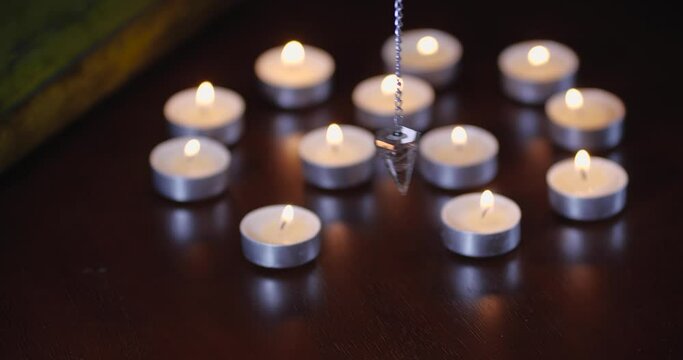Close-up detailed shot of crystal pendulum hovering over table with candles  on black background with smoke. Dowsing. Predicting future or Halloween concept