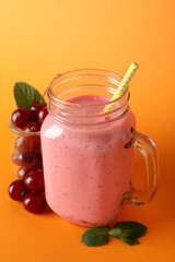 Glass jar of cherry smoothie and ingredients on orange background