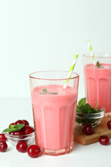 Glasses of cherry smoothie and ingredients on white table