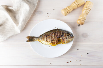 Grilled dorado fish stuffed with lemon on a light wooden table.