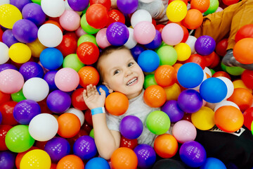 Boy kid playing and having a good time in a ball room. Little smiling child playing lying in colorful balls park playground. Happy boy having fun jumping into the ball pit with colorful balls.