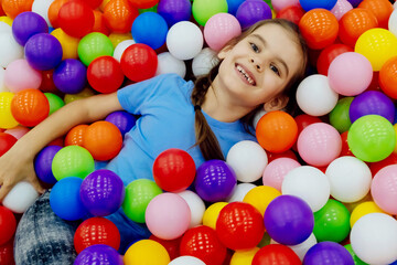 Fototapeta na wymiar Happy girl kid having fun in ball pit with colorful balls. concept of safety in shopping centers, hygiene in the children's room.