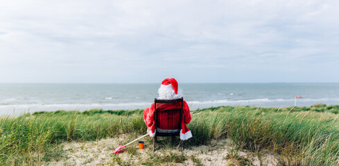 back view of Santa Claus on a trip to the sea enjoying the view from a dune sitting on a deckchair