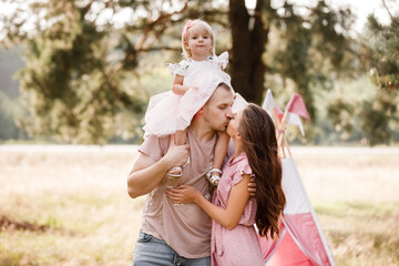 The daughter hugging parents on nature. Mom, dad and girl toddler, walk in the park. Happy young...