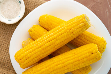 corn cooked on the cob on a white plate, next to a salt shaker with salt