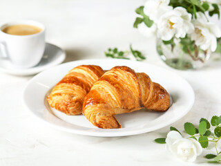 Serving breakfast on a marble table. Croissants on a white plate. French cuisine. Pastries, coffee and white flowers. It's a beautiful morning. French-style breakfast for a girl