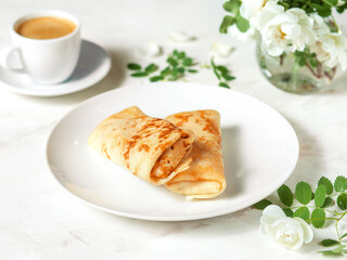 Serving breakfast on a marble table. Crepes on a white plate. French cuisine. Pastries, coffee and white flowers. It's a beautiful morning. French-style breakfast.