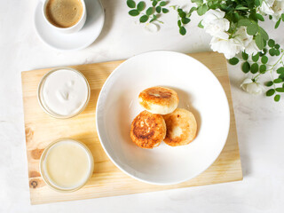 Serving breakfast on a marble table. Cottage cheese with topping on a white plate. Pastries, coffee and white flowers.  French-style breakfast. Mini cheesecakes with sour cream.