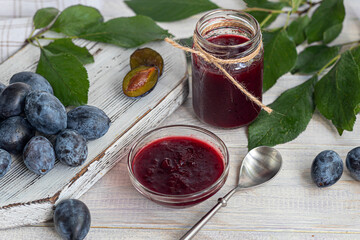 Plum jam in a jar. In the background there are plums. Tkemali sauce. Preparing for winter. Light background.