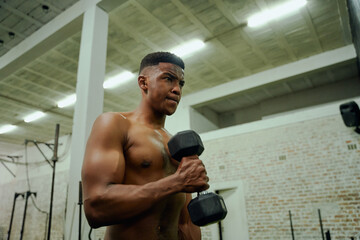 African American male holding weights during an intense workout. Male athlete looking at himself in the gym mirror while lifting dumbbells. High quality photo