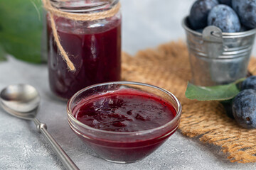 Plum jam in a jar. In the background there are plums. Tkemali sauce. Preparing for winter. Light background.