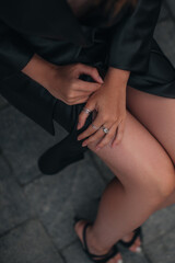 Female hands with silver rings lying on slender legs. Female body in a fashionable black leather jacket, skirt. Street style