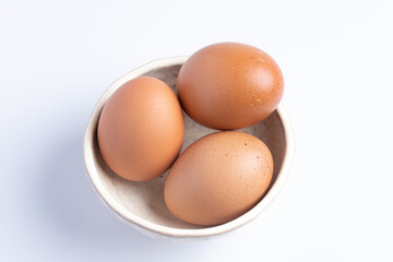 Three fresh eggs in a cup on a white background.