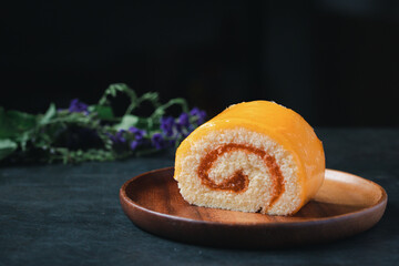 Orange roll cake in wooden plate on black background