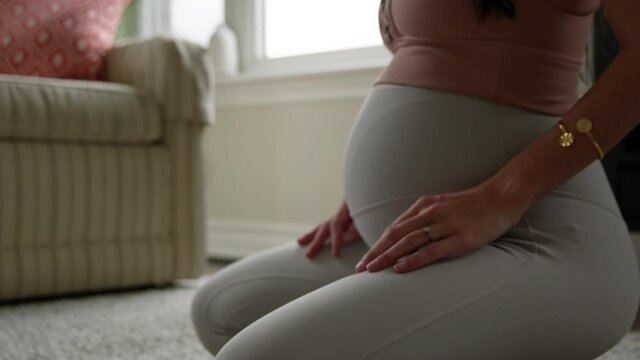 Pregnant woman 25 weeks pregnant meditates as she kneels down - close up on hands and belly