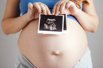 pregnant belly woman on grey studio background holding in hands card with ultrasound black and white scan, pregnancy concept