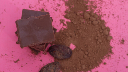 Chocolate, cocoa beans, cocoa powder on a pink background